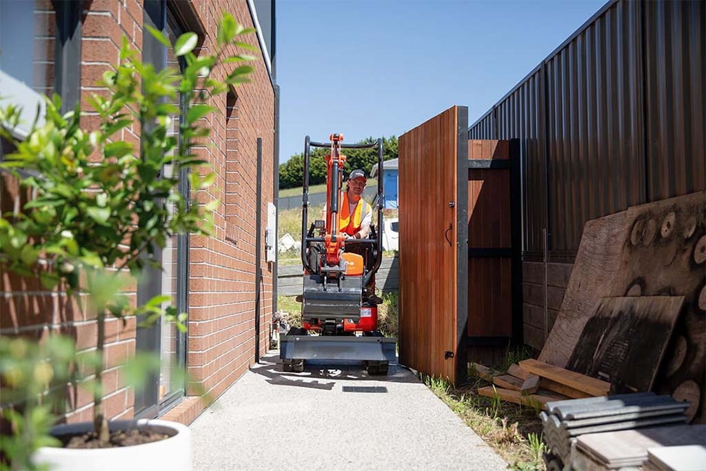 Mini excavator squeezing through a side gate